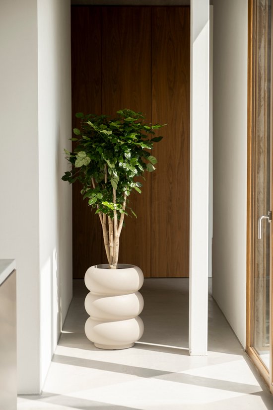 Een grote plantenbak in off-white met een bolvormig, gestapeld design met een groene plant, in een moderne hal.
