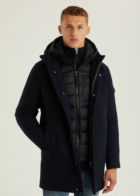 Man in donkerblauwe wollen parka met capuchon, met een zwarte pufferjas eronder.