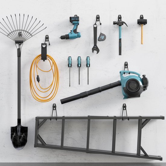 Een assortiment aan gereedschap, waaronder een bladblazer, boormachine, schroevendraaiers, hark, schep, ladder en gereedschapshaken, hangend aan een witte muur.