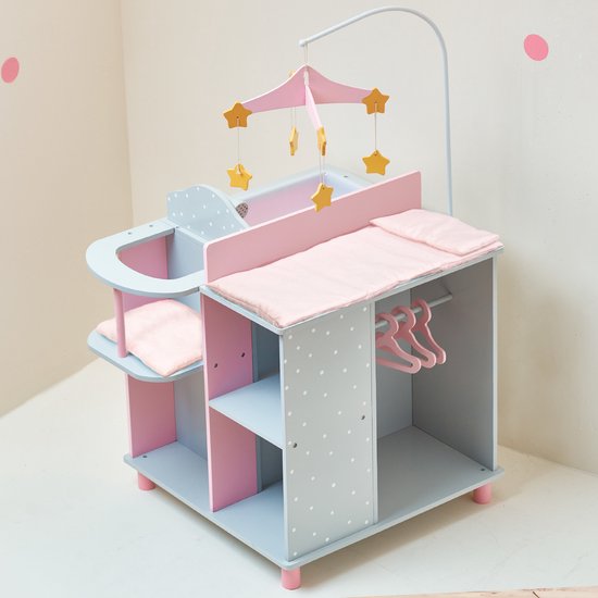 Grijze commode met roze en lichtblauwe vakken, witte stippen. Commodeblad met roze matras, badje met douchekop, mobiel met gele sterren.