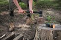 Man met bruine laarzen slijpt een bijl op een boomstronk met een Fiskars slijper naast zich.