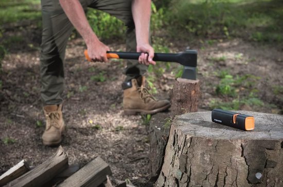 Man met bruine laarzen slijpt een bijl op een boomstronk met een Fiskars slijper naast zich.