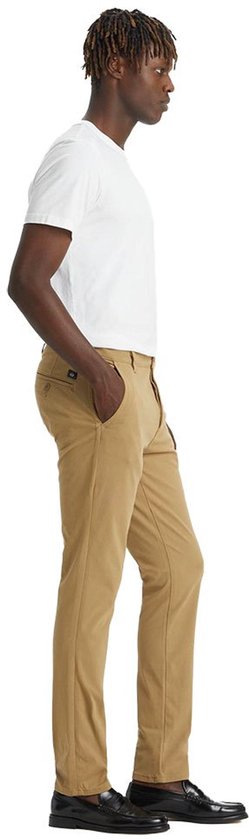 Man in een beige chino broek, staand met de hand in de zak.