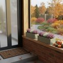 Twee grijze houten bloembakken met roze en witte heide, op een bakstenen vensterbank, met pompoenen en herfstbladeren.