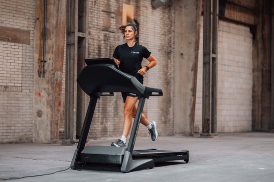 Vrouw met paardenstaart rent op een loopband in zwart Focus Fitness shirt en zwarte broek.