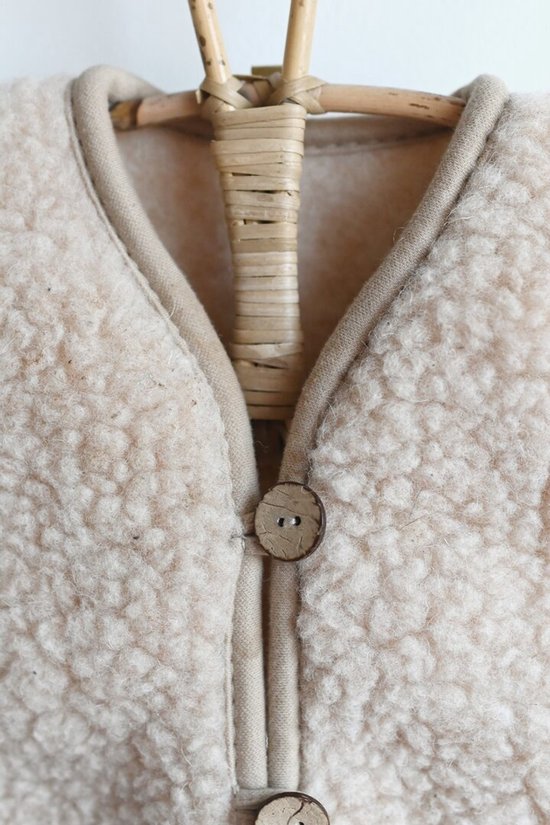 Crèmekleurig wollen kinder vest met bruine houten knopen, close-up van de kraag.