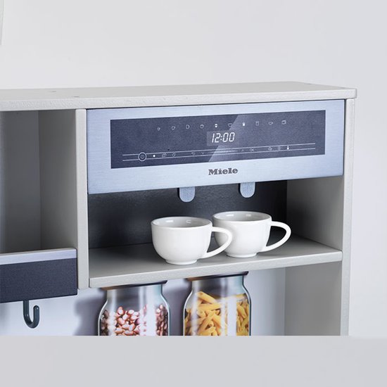 Miele speelgoedkeuken met zilverkleurige bovenkast en digitaal display, twee witte mokken ernaast.