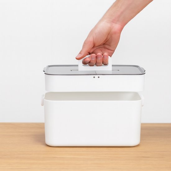 Hand pakt het witte handvat van de transparant grijze deksel, boven een witte opbergdoos.