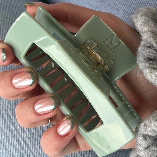 Hand met groene nagellak houdt een lichtgroene, rechthoekige haarklem met logo.