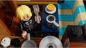 LEGO minifiguur met blonde haren, zwart pak, met vork en mok, in een keuken setting.