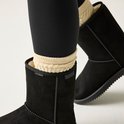 Dames voeten in zwarte laarzen met beige gebreide sokken. De laarzen hebben een merklogo en 'WATERPROOF' opdruk.