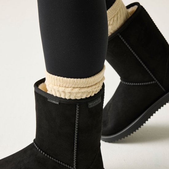 Dames voeten in zwarte laarzen met beige gebreide sokken. De laarzen hebben een merklogo en 'WATERPROOF' opdruk.