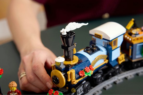 Close-up van de blauwe LEGO-trein met gouden details en kerstdecoratie, bij een rokende schoorsteen.