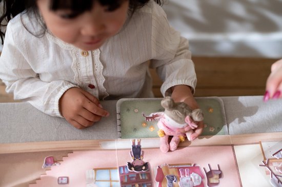 Meisje speelt met een stoffen pop op een kartonnen speelset, met kamers en accessoires.