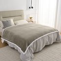 Taupe fleece plaid met witte sherpavoring, gedrapeerd over een bed.