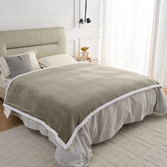 Taupe fleece plaid met witte sherpavoring, gedrapeerd over een bed.