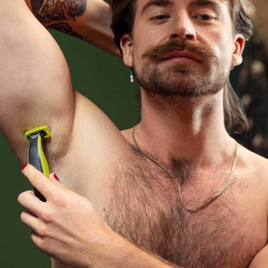 Man met snor gebruikt gele OneBlade trimmer onder zijn oksel.
