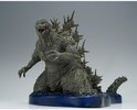 Grijze Godzilla figuur met scherpe rugplaten, knielend op een blauwe waterbasis.
