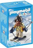Playmobil skiër met baard, skibril, gele jas met luipaardprint, beige broek en blauwe wanten, op ski's.