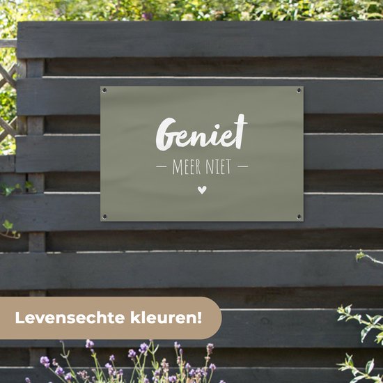 Donkergroene banner met witte tekst 'Geniet - Meer Niet -' en een hartje, hangend aan een donkerhouten schutting.