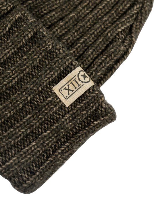 Detail van een donkergroene gebreide muts met ribbelpatroon en label.