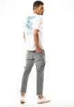 Man in witte t-shirt met blauwe print op de rug en grijze jeans, draait zich om.