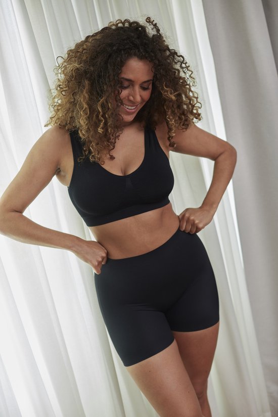 Model met krullend haar, lachend, met zwarte sport BH en zwarte body short.