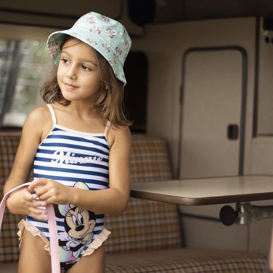 Meisje met strikjesmuts draagt een gestreept Minnie Mouse badpak, staand bij een camper.