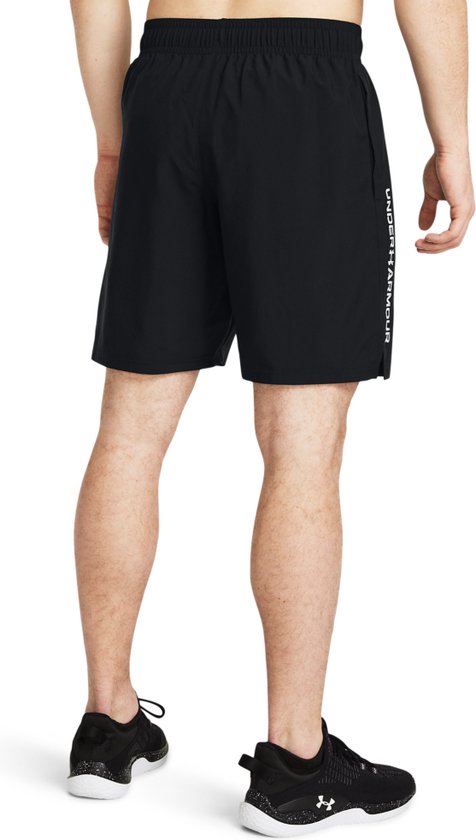 Achterkant van een man in een zwarte sportbroek met 'Under Armour' logo op de zijkant.