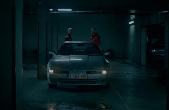 Twee mannen praten in parkeergarage bij zilverkleurige sportauto.