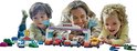 Une femme et deux enfants sont allongés sur le sol et jouent avec une piste de course LEGO Duplo.