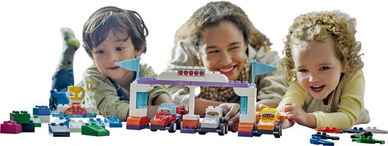 Une femme et deux enfants sont allongés sur le sol et jouent avec une piste de course LEGO Duplo.