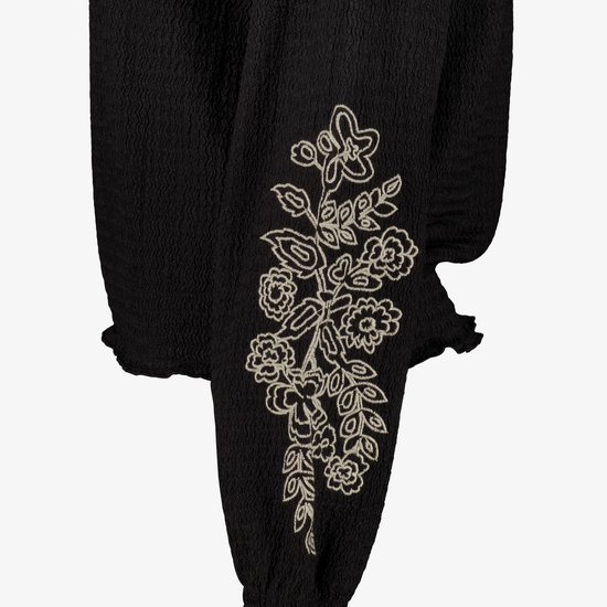 Detail van de geborduurde bloemen op de mouw van een zwarte blouse.