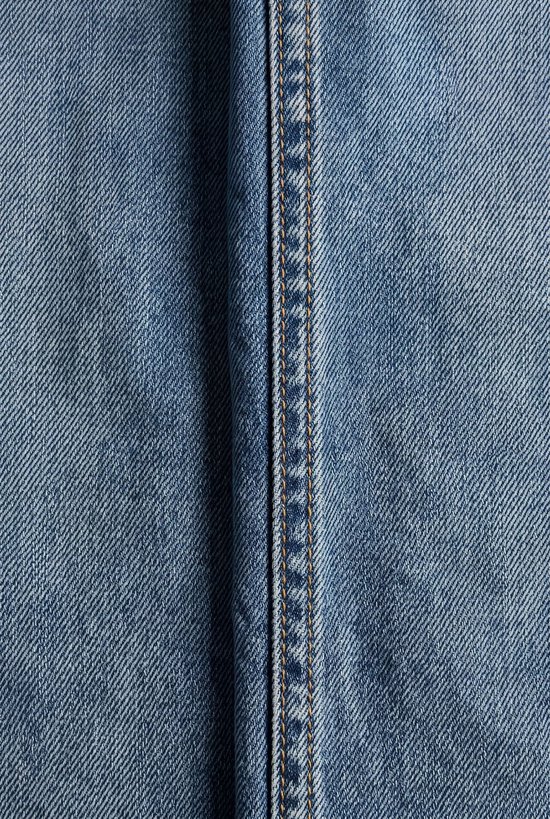 Sluiting van een lichtblauwe jeans met een dubbele naad en gele stiksels.