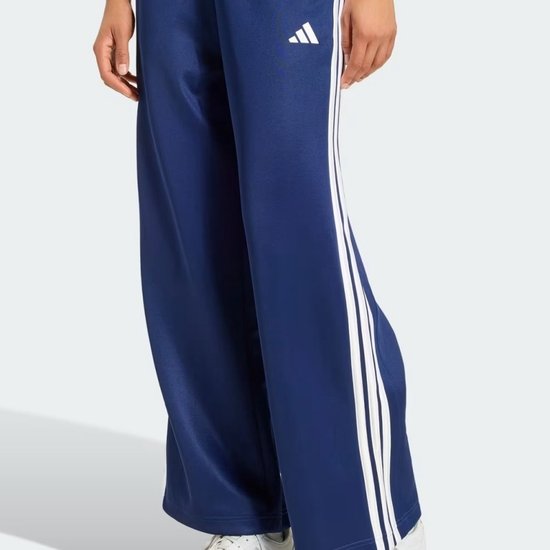 Model draagt een wijde donkerblauwe adidas trainingsbroek met witte strepen aan de zijkant en een adidas-logo.