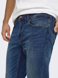 Close-up van de taille en heup van een blauwe jeans met koperkleurige knopen en contrasterende stiksels.