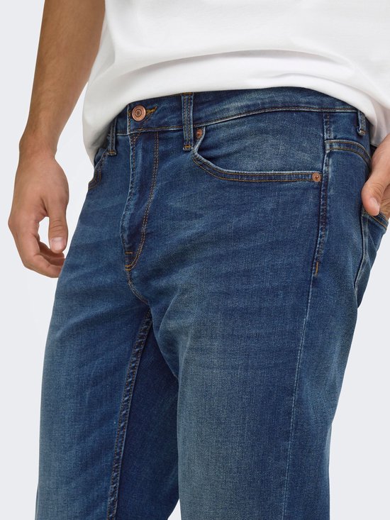 Close-up van de taille en heup van een blauwe jeans met koperkleurige knopen en contrasterende stiksels.