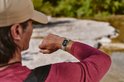 Persoon draagt een lichtgroene Fitbit Edge, kijkend naar het scherm bij een stroompje.
