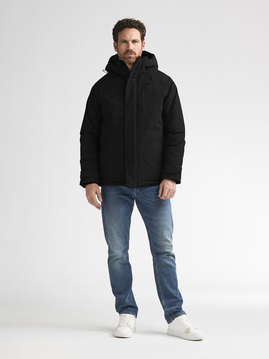 Model draagt zwarte parka met capuchon, blauwe jeans en witte sneakers.