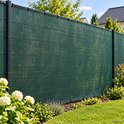 Groen schaduwnet bevestigd aan donkergrijze palen, langs een tuin.