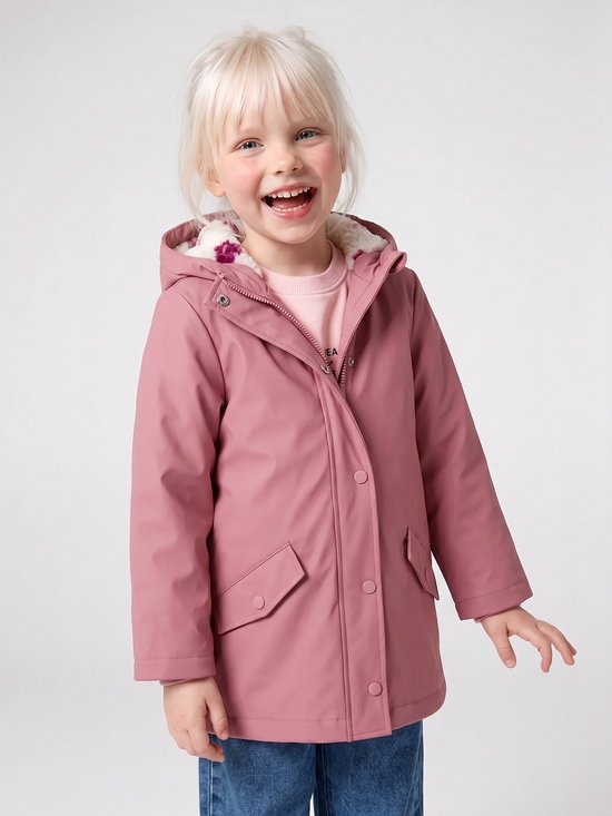 Meisje met blond haar, lachend, draagt een roze regenjas met teddy voering en spijkerbroek.