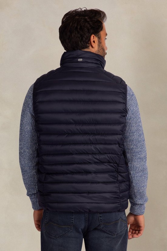 Donkerblauwe gewatteerde bodywarmer met hoge kraag, gedragen over een blauw gebreid vest.