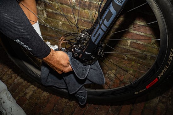 Een hand veegt met een doek de remschijf van een fiets schoon.