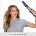 Vrouw houdt een grijze föhnborstel vast en droogt haar haar snel en gemakkelijk.