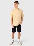 Model draagt een beige T-shirt met Brunotti-logo en zwarte denim shorts met opgerolde zomen.