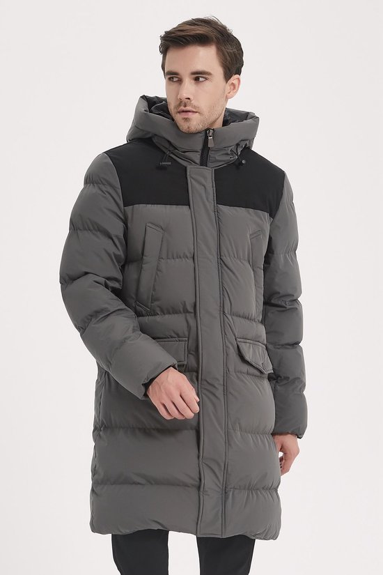 Model draagt een lange grijze gewatteerde jas met capuchon en zwart detail op de schouders.