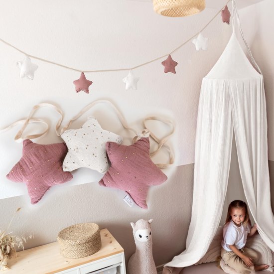 Roze en witte sterrenslinger van mousseline met gouden stippen in een kinderkamer met een witte hemel.