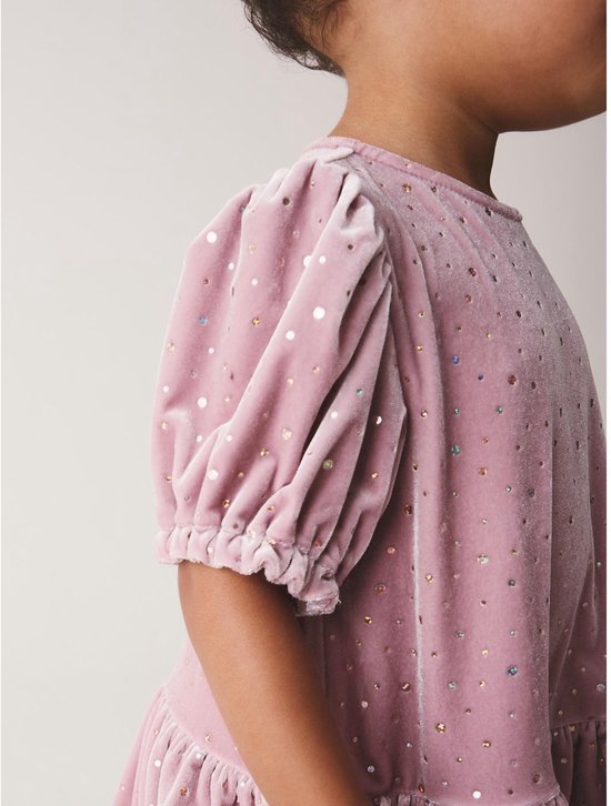 Close-up van de roze fluwelen jurk met glinsterende stippen en pofmouwen.