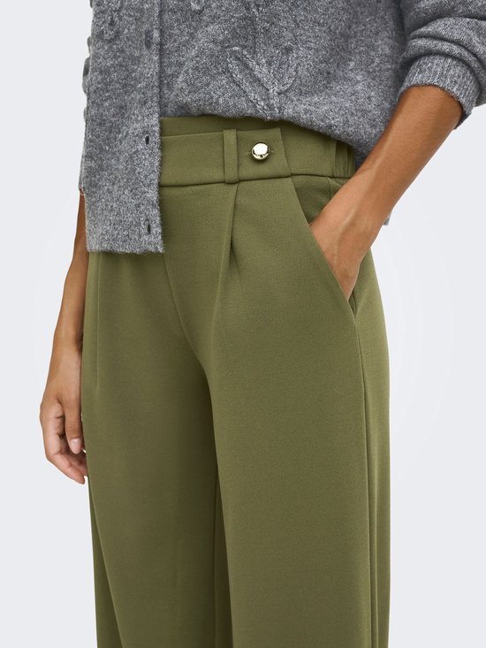 Close-up van een olijfgroene broek met wijde pijpen, met een zilveren knoopdetail op de tailleband.
