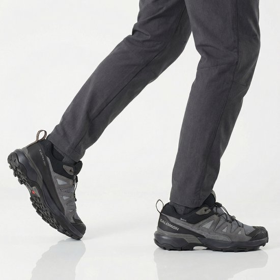 Man die in grijze Salomon X ULTRA 360 wandelschoenen loopt, met donkergrijze broek.